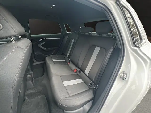 Vue intérieure arrière droite de l'Audi A3 Sportback 2024 blanc Arkona, sièges tissu noir avec bandes grises.