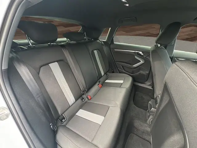 Vue intérieure arrière côté droit de l'Audi A3 Sportback blanc Arkona, sièges tissu noir avec bandes grises centrales.