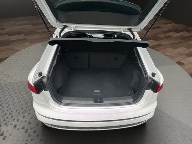 Vue arrière d’un Audi A3 Sportback blanc Arkona 2024 avec coffre ouvert et intérieur de coffre noir visible.
