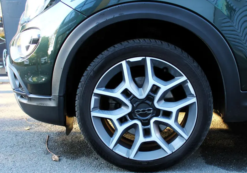 Gros plan sur la roue avant gauche d'une FIAT 500X vert Toscane métal, mettant en valeur la jante alu au design moderne.