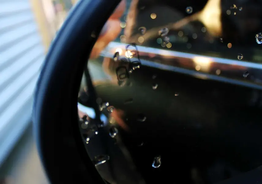 Gros plan sur la poignée chromée et la vitre arrière d'une FIAT 500X vert Toscane sous gouttes d'eau.