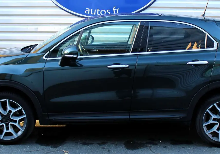 Profil côté gauche d'une FIAT 500X vert Toscane métal 2019 avec jantes alliage et attelage visible.