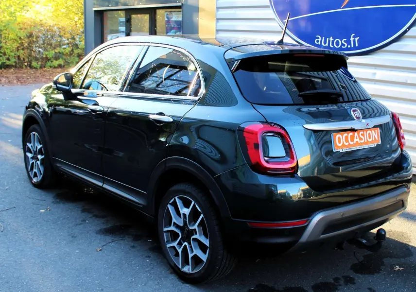 Vue 3/4 arrière droite d'une Fiat 500X vert Toscane métallisé avec attelage et jantes alliage biton.