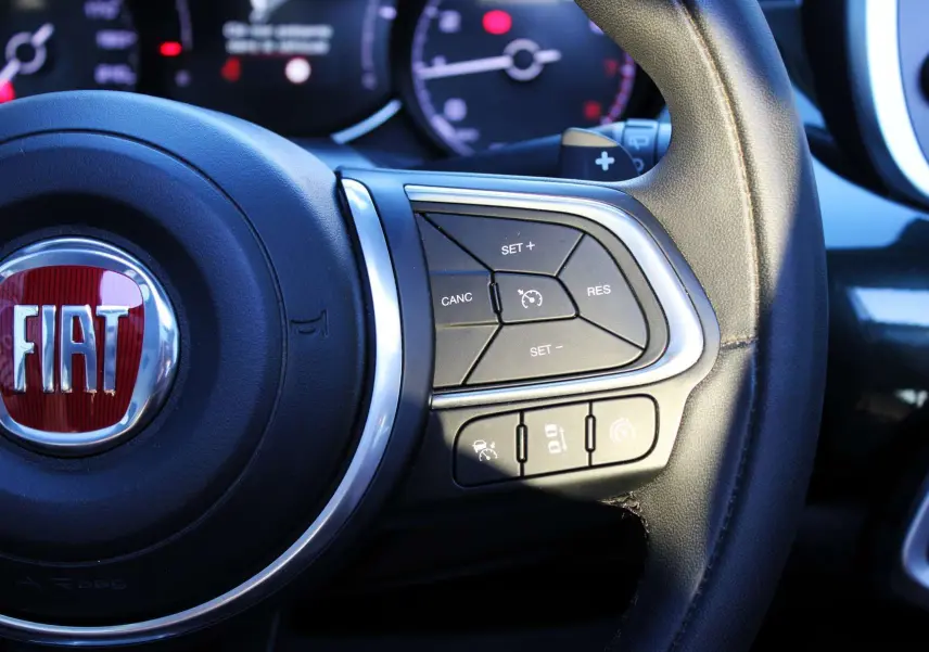 Gros plan sur le volant en cuir noir avec commandes intégrées et logo FIAT rouge du 500X 2019.