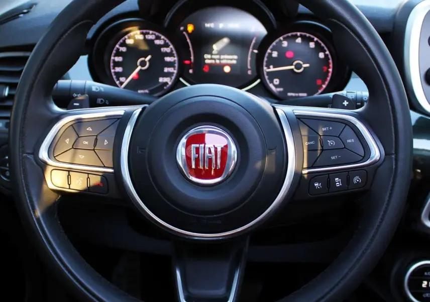 Vue rapprochée du volant noir de la Fiat 500X avec logo rouge et tableau de bord numérique en arrière-plan.