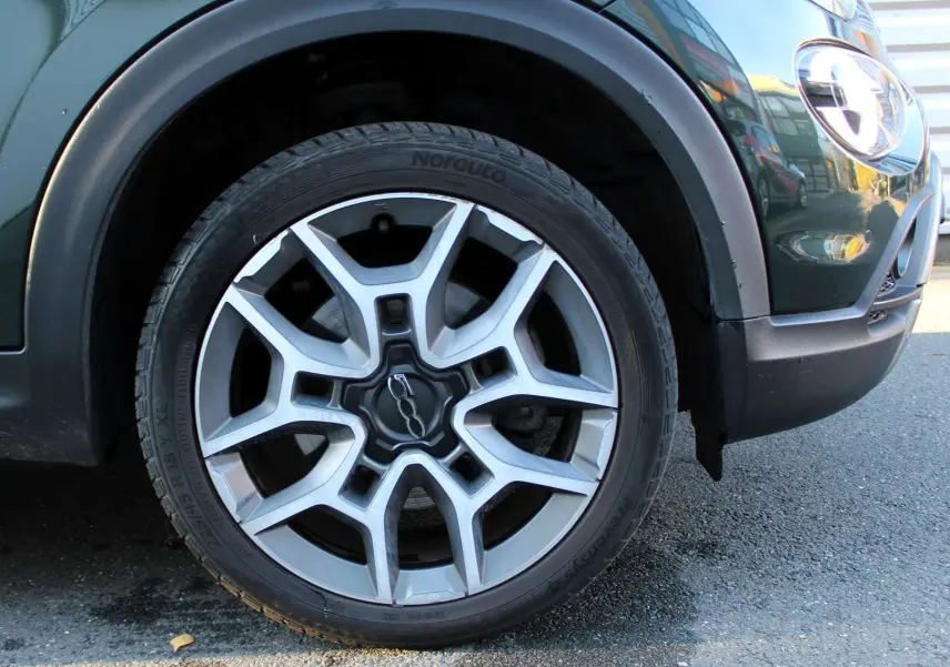 Gros plan sur la roue avant gauche d'une FIAT 500X vert Toscane métal avec jante alliage et partie avant du pare-chocs visible.