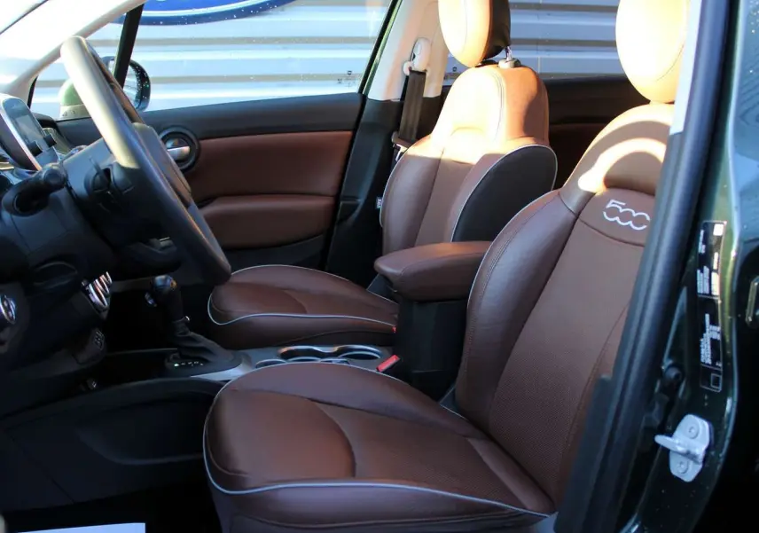 Vue intérieure côté conducteur de la Fiat 500X 2019 avec sièges cuir marron et détails verts Toscane métal.