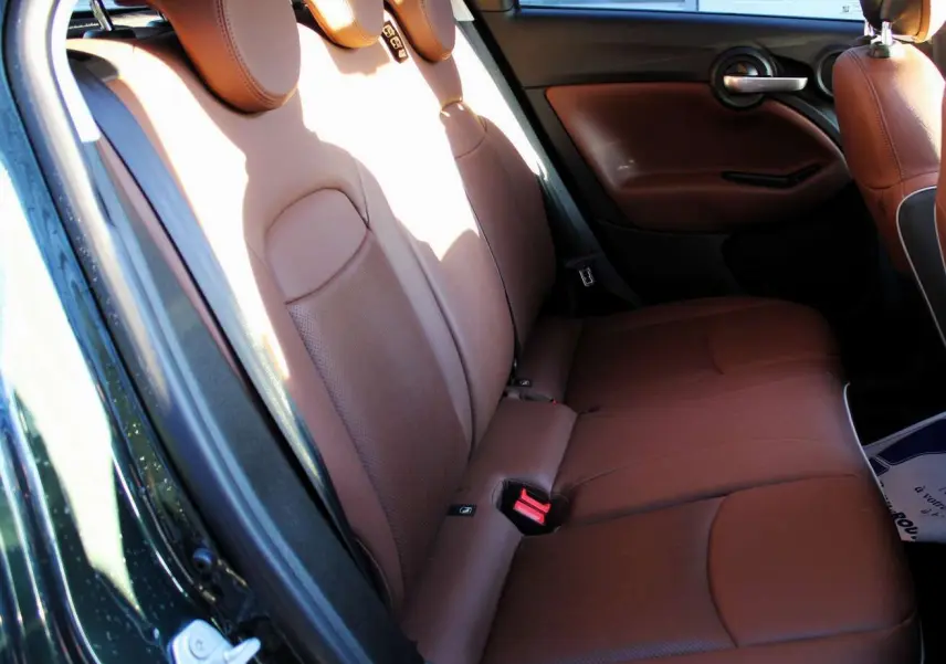 Vue intérieure arrière gauche des sièges en cuir marron du Fiat 500X 2019 vert Toscane, avec garnitures de porte assorties.