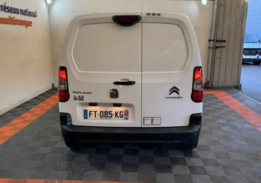 Vue arrière d’un utilitaire Citroën Berlingo blanc, avec feux arrière allumés et plaque d’immatriculation visible.