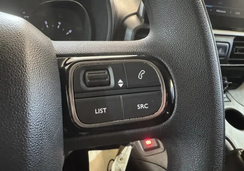 Gros plan sur les commandes multifonctions noires du volant d’un Citroën Berlingo blanc, intérieur côté conducteur.