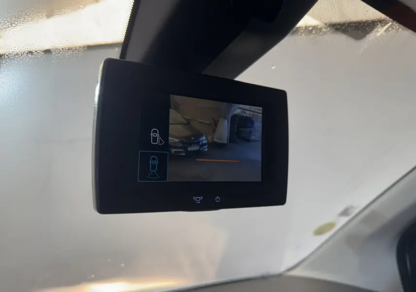 Écran de rétroviseur caméra intérieur affichant une vue arrière partielle d’un véhicule noir en parking.