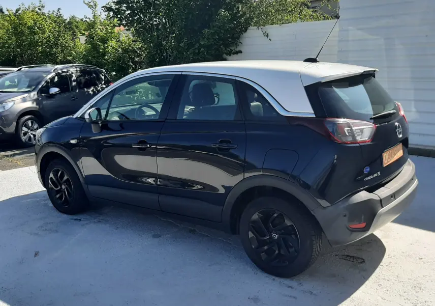 Opel Crossland noir avec toit blanc vu de trois quarts arrière droit, stationné en extérieur au soleil.