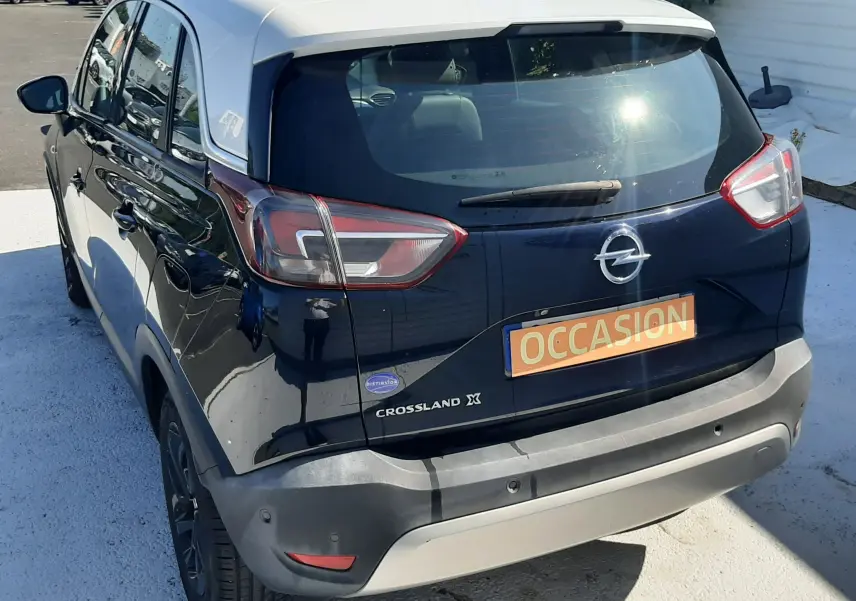 Vue 3/4 arrière droite d'un Opel Crossland noir avec toit blanc, immatriculé en occasion, sur parking extérieur.