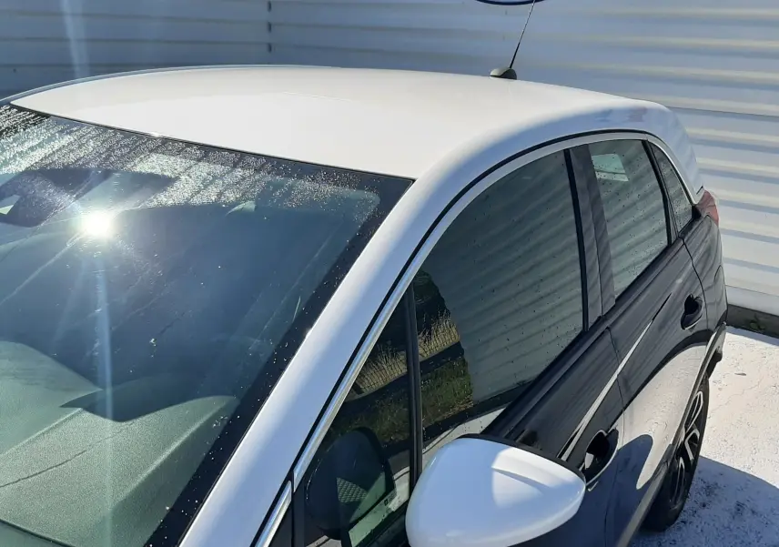 Vue de côté droit en plongée d'un Opel Crossland noir avec toit et rétroviseur blanc, stationné devant un mur publicitaire.