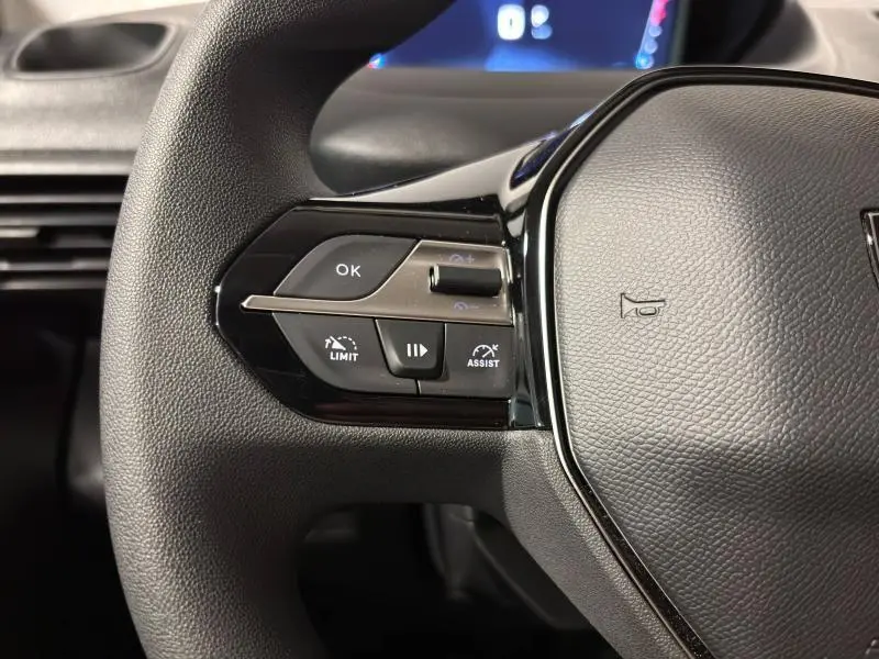 Gros plan sur le volant noir du Peugeot Partner 2025, montrant les commandes multifonctions côté gauche avec boutons OK, Limit et Assist