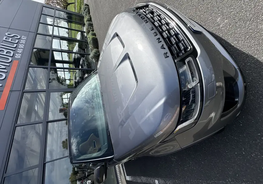 Vue 3/4 avant droit d'un Range Rover Sport SVR Carbon Edition gris foncé garé devant un bâtiment vitré.