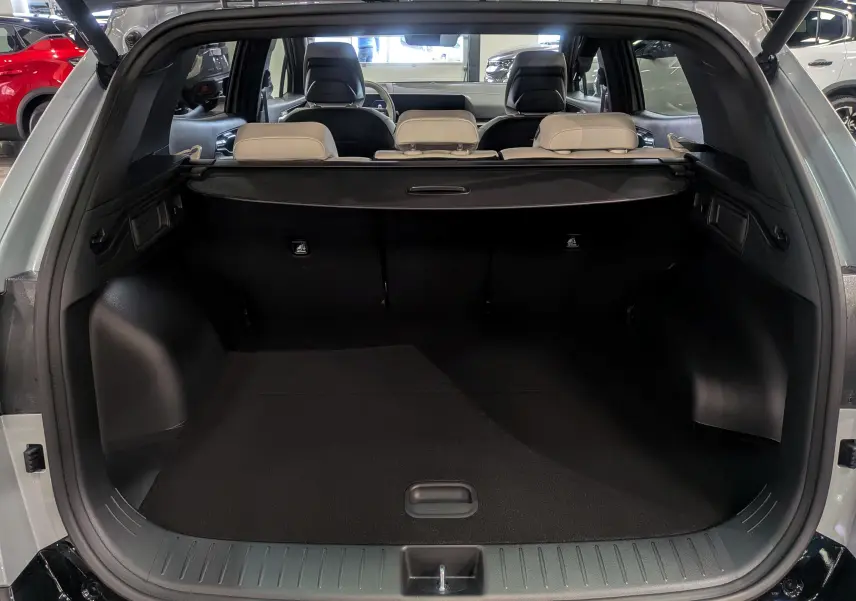 Coffre ouvert du Kia Sportage 2025 gris céramique avec intérieur noir et sièges arrière beiges visibles.
