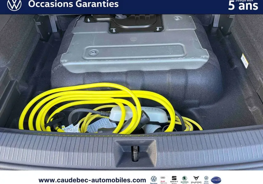 Coffre ouvert d’un Volkswagen Tiguan argent Dolomite avec câble de recharge électrique jaune visible.