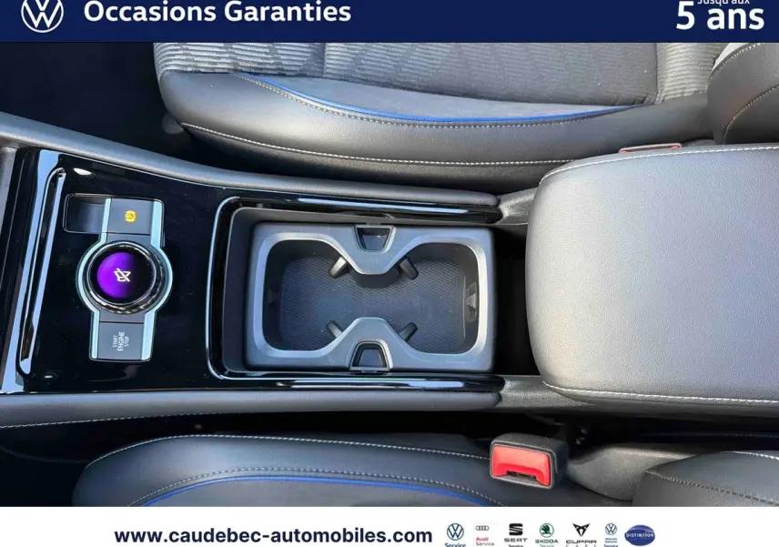Vue plongeante sur la console centrale noire brillante du Volkswagen Tiguan eHybrid avec porte-gobelets et accoudoir gris.