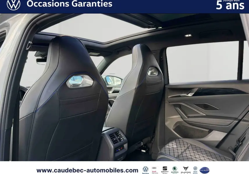 Vue intérieure arrière du Volkswagen Tiguan eHybrid 2025, sièges sport noirs avec surpiqûres bleues et toit ouvrant panoramique.