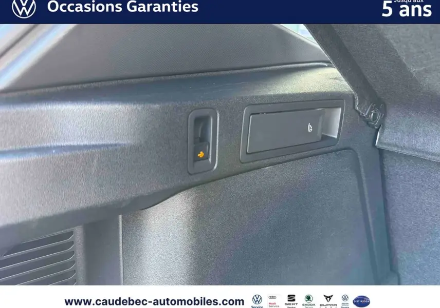 Détail intérieur du coffre du Volkswagen Tiguan eHybrid 2025 montrant les commandes de rabattement des sièges arrière.