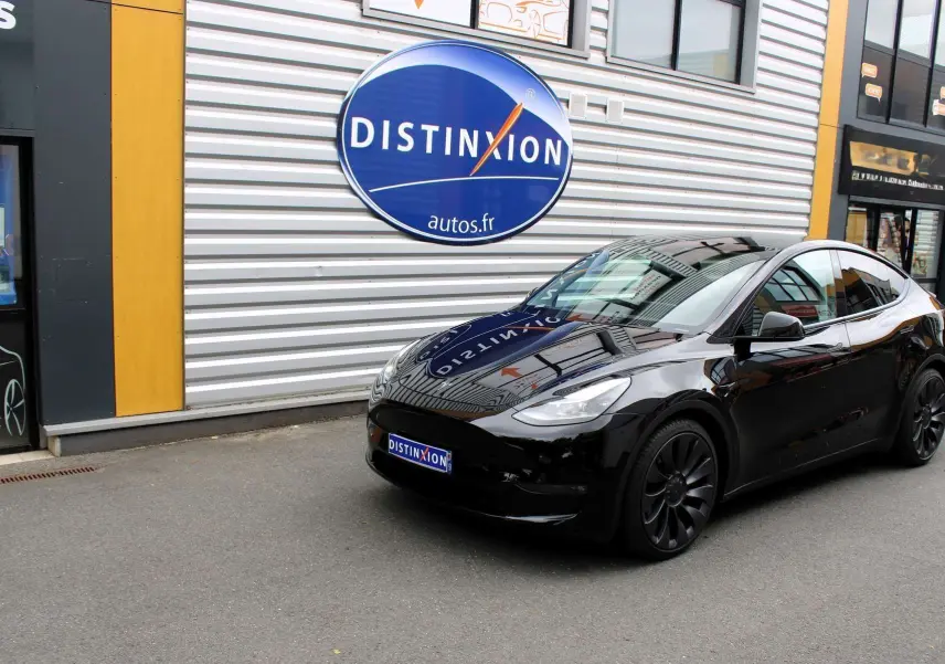 Tesla Model Y noir métal vue 3/4 avant droit, garée devant un bâtiment avec logo Distinxion visible.