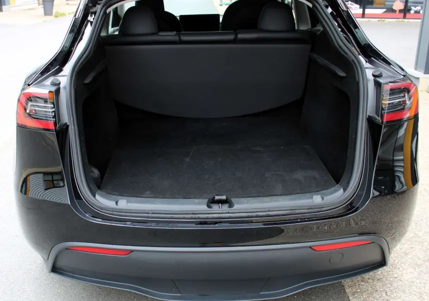 Coffre ouvert vu de l'arrière d'une Tesla Model Y noire métal 2024, soulignant l'espace de chargement vide et le hayon relevé.