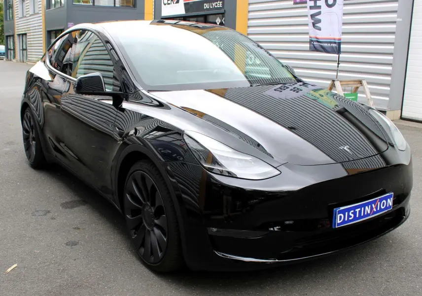 Tesla Model Y noir métal en vue 3/4 avant gauche, avec jantes noires et calandre lisse distinctive électrique.
