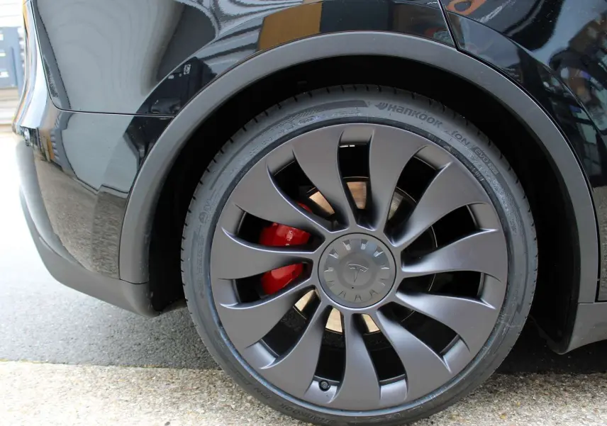 Gros plan sur la roue arrière droite noire métallisée d'une Tesla Model Y 2024 avec étrier de frein rouge visible.