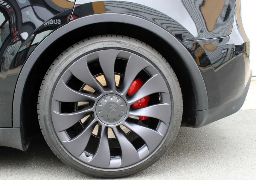 Gros plan sur la roue arrière droite noire métallisée d'une Tesla Model Y 2024 avec étrier de frein rouge visible.