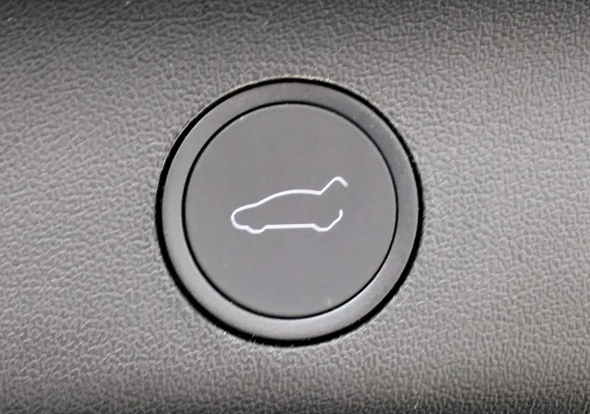 Bouton noir avec icône blanche de hayon ouvert, détail intérieur du Tesla Model Y noir métal 2024.