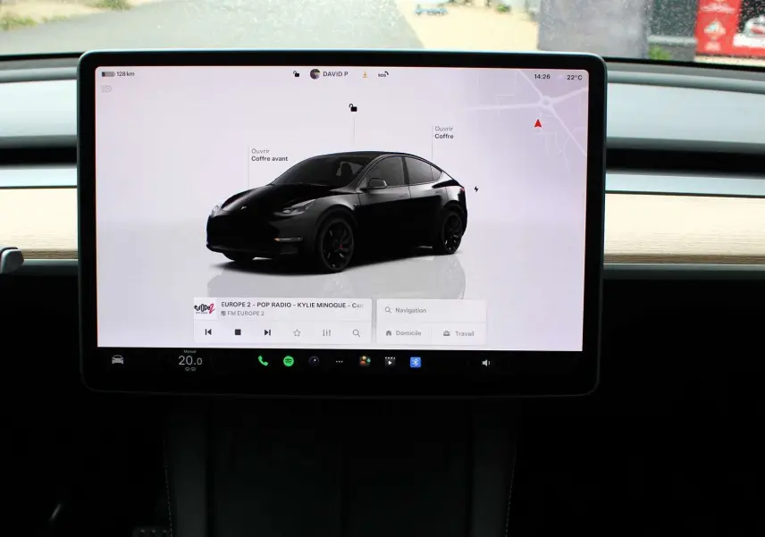 Écran tactile central affichant une Tesla Model Y noir métal en 3/4 avant sur fond blanc, avec options de contrôle visibles.
