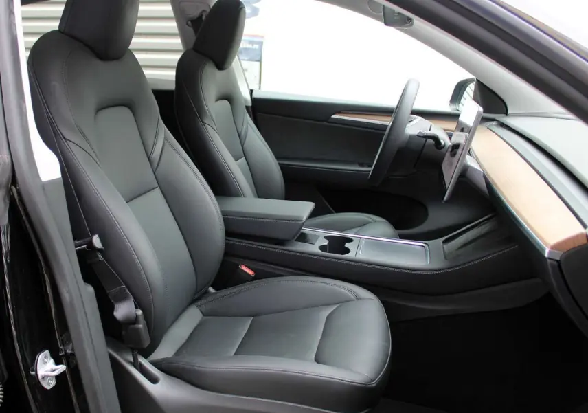 Intérieur de la Tesla Model Y 2024 noir métal, vue côté gauche sur sièges cuir noir et tableau de bord bois clair.