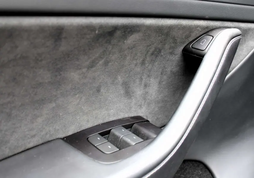 Détail de la poignée intérieure côté gauche en cuir noir et commandes de vitres de la Tesla Model Y Performance 2024.