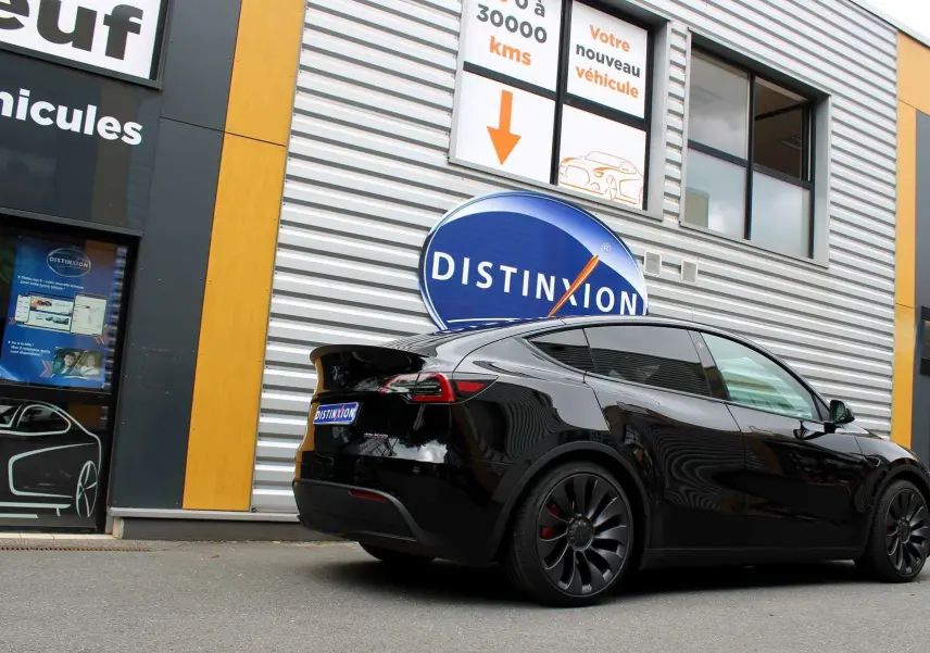 Tesla Model Y Performance noir métal en 3/4 arrière droit, stationné devant un bâtiment avec enseigne Distinxion.