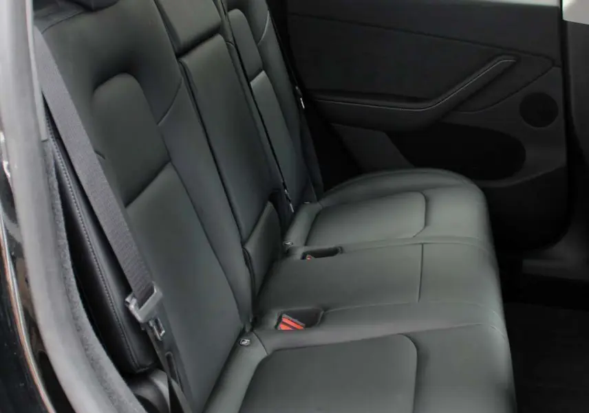 Vue latérale du siège arrière en cuir noir de la Tesla Model Y 2024, avec ceinture de sécurité et porte côté droit visible.
