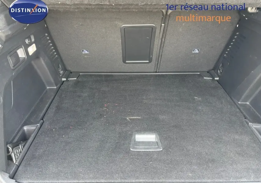 Coffre spacieux et propre du Peugeot 3008 GT blanc nacré, vue intérieure arrière avec tapis noir et rangements latéraux.