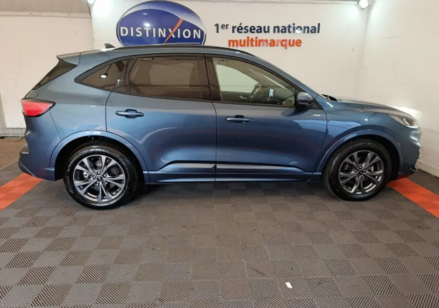 Ford Kuga 2024 bleu en profil côté gauche, avec jantes alliage et vitres teintées dans un showroom.