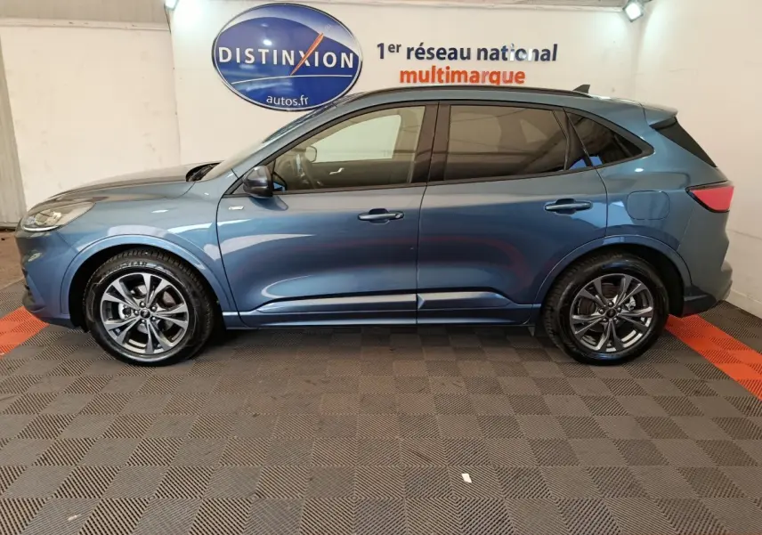 Profil côté gauche du Ford Kuga 2024 bleu St Line avec jantes alliage et vitres teintées en intérieur showroom