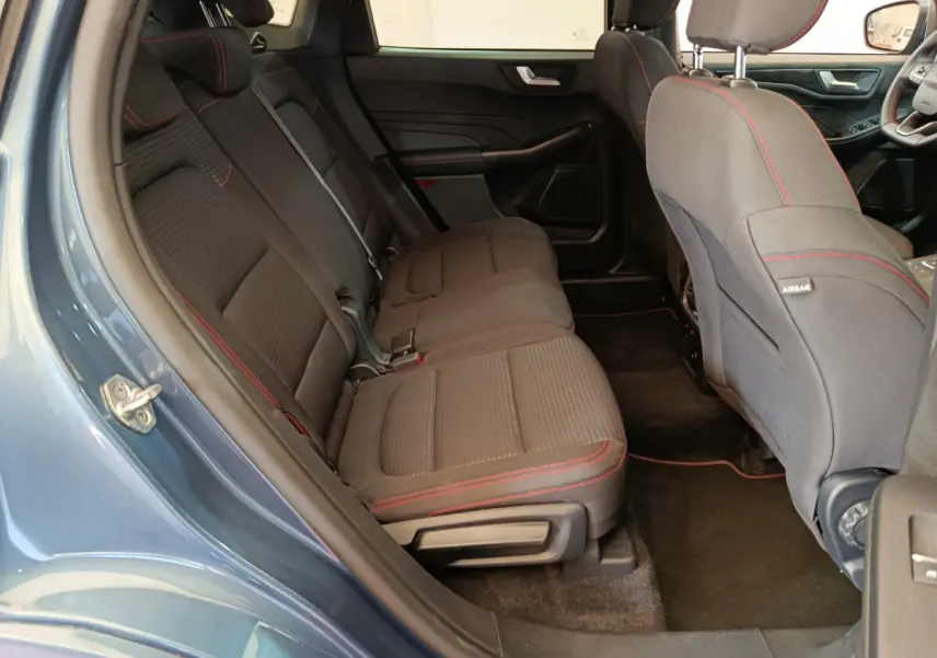 Vue intérieure côté gauche sur la banquette arrière noire avec surpiqûres rouges du Ford Kuga 2024 bleu St Line.