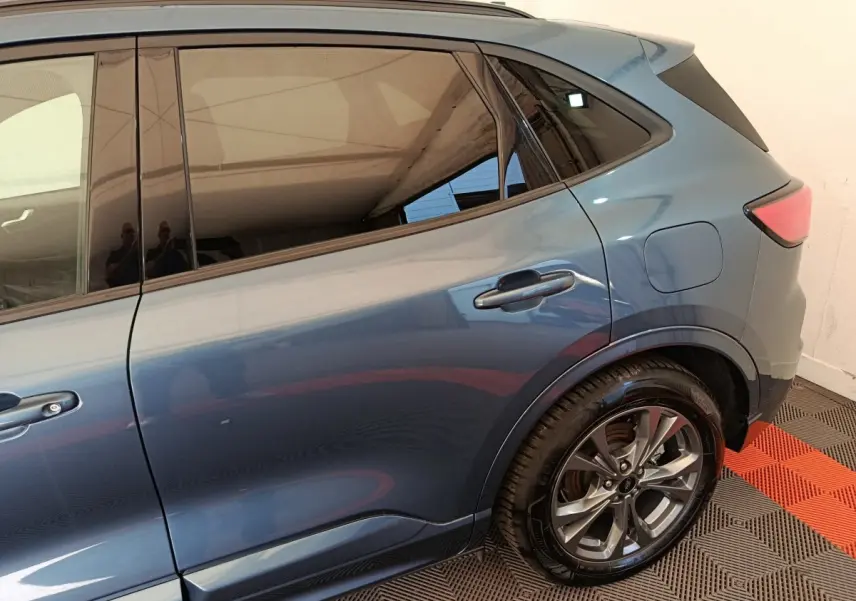 Vue latérale droite du Ford Kuga bleu 2024, mettant en valeur la porte arrière et la roue alliage au design moderne.