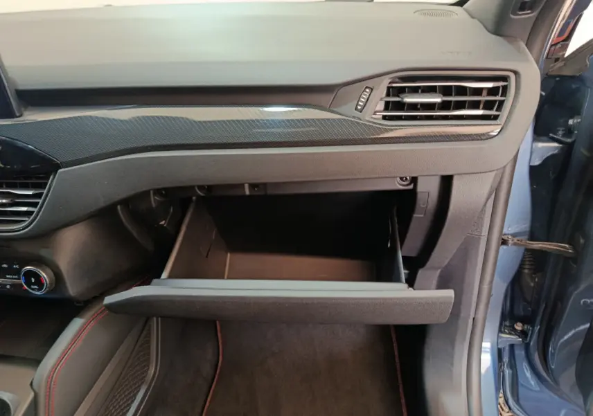 Intérieur côté passager du Ford Kuga bleu 2024, boîte à gants ouverte sous la planche de bord noire avec surpiqûres rouges.