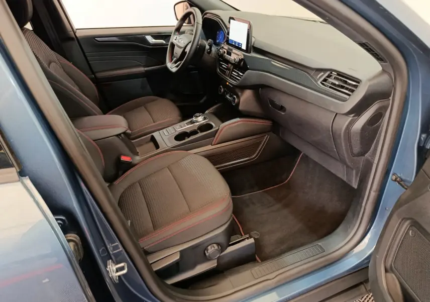Intérieur avant droit du Ford Kuga bleu 2024 avec sièges noirs surpiqués rouges et écran tactile central.