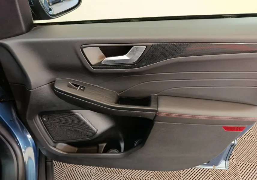 Intérieur côté gauche de la porte avant d'un Ford Kuga bleu 2024 avec garniture noire et surpiqûres rouges.
