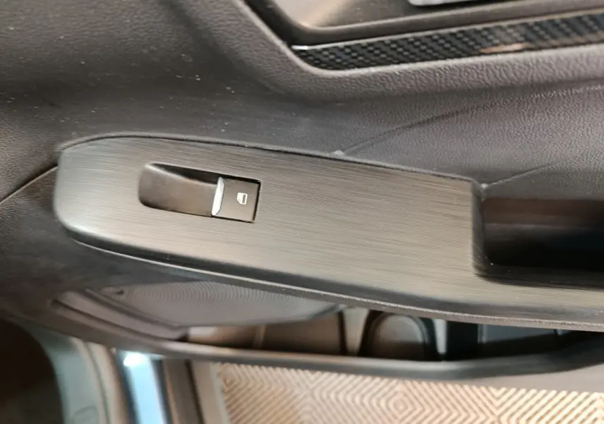 Gros plan sur la commande de lève-vitre côté gauche dans l'habitacle du Ford Kuga bleu 2024 St Line.