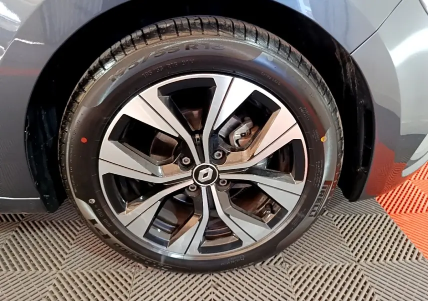 Gros plan sur la roue avant gauche d'une Renault Clio gris foncé, mettant en valeur la jante alliage au design moderne.