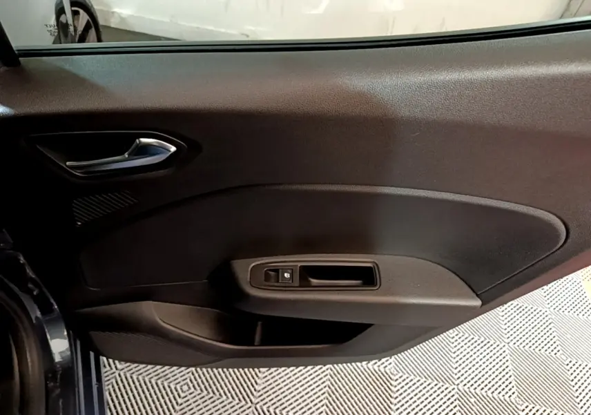 Vue intérieure sur la porte côté conducteur de la Renault Clio gris foncé, avec poignée et commande de vitre électrique.