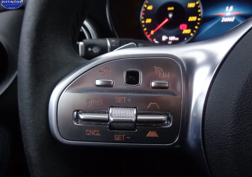 Gros plan sur les commandes argentées au volant d'une Mercedes Classe C Break 220D noir métal, tableau de bord en arrière-plan.