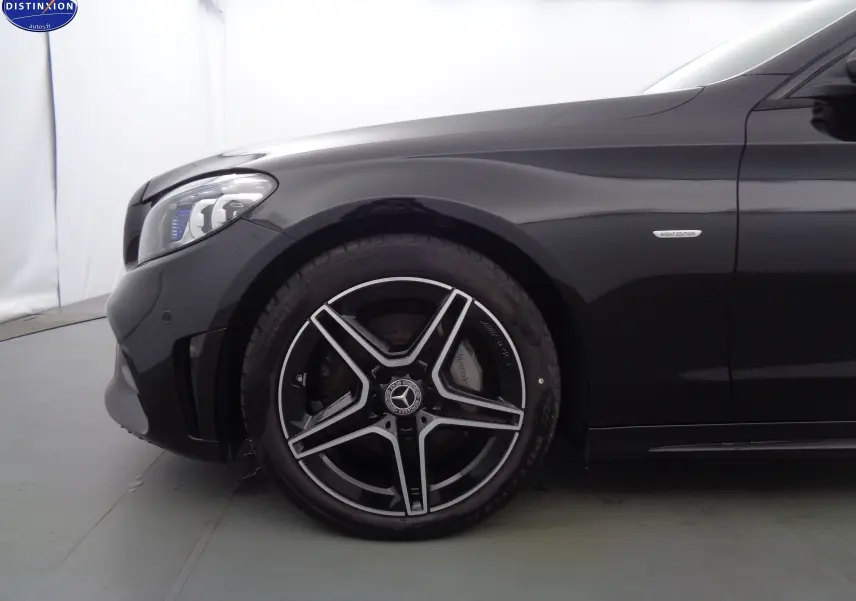 Gros plan sur la roue avant gauche et l'aile noire métallisée d'une Mercedes Classe C Break 220D AMG Line avec badge Night Edition.