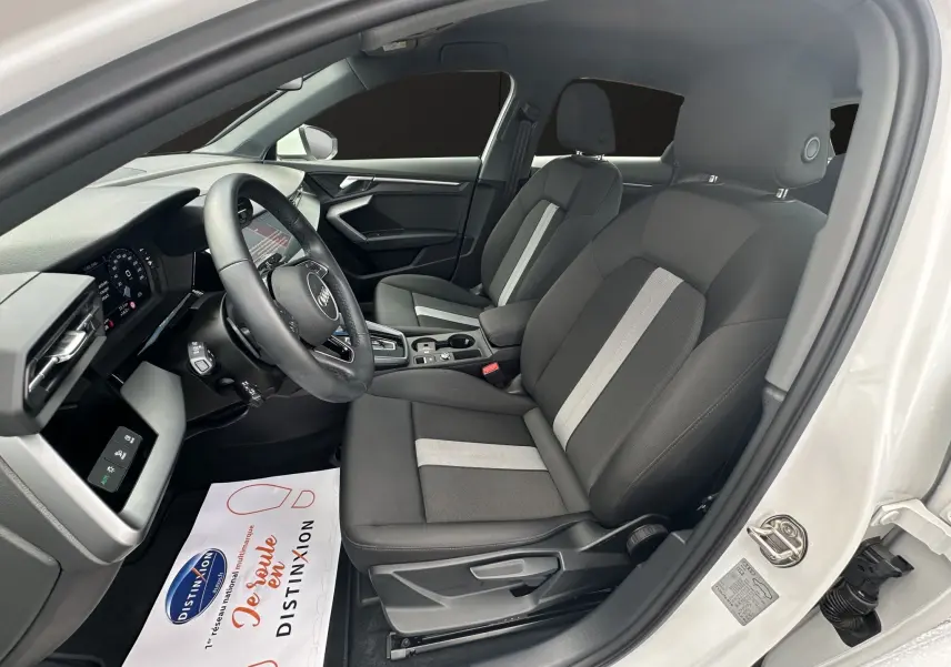 Intérieur côté conducteur d'une Audi A3 Sportback blanche, sièges tissu noir avec bande grise centrale et volant cuir multifonctions.